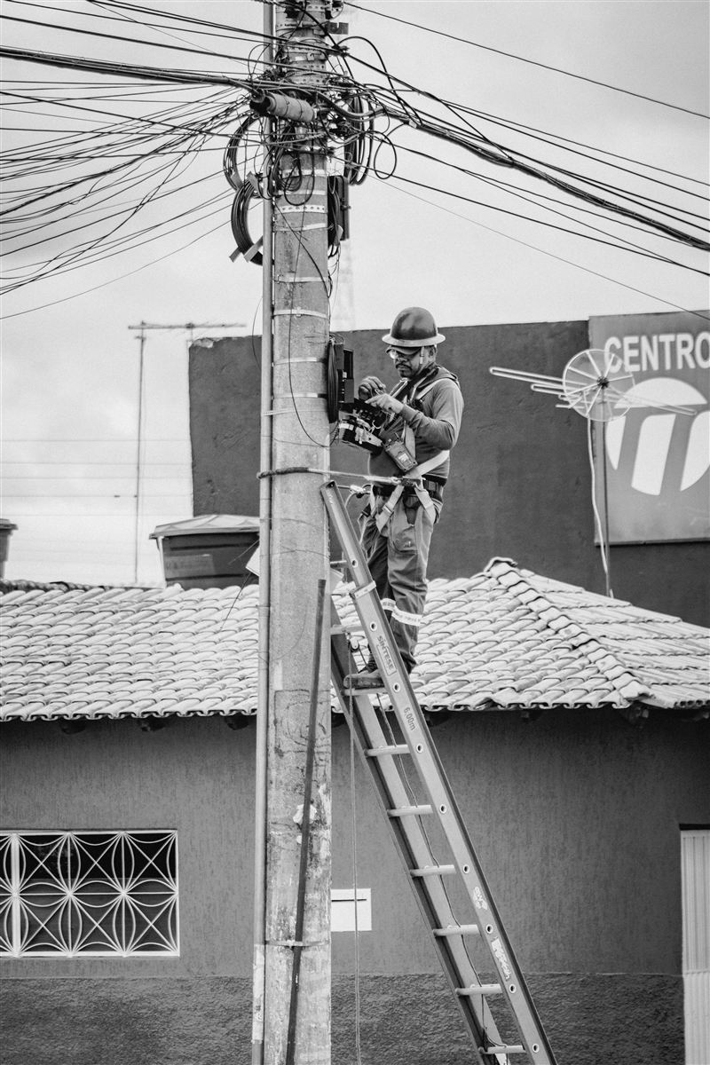 Eletricista trabalhando em poste de rede de distribuição com equipamentos de segurança