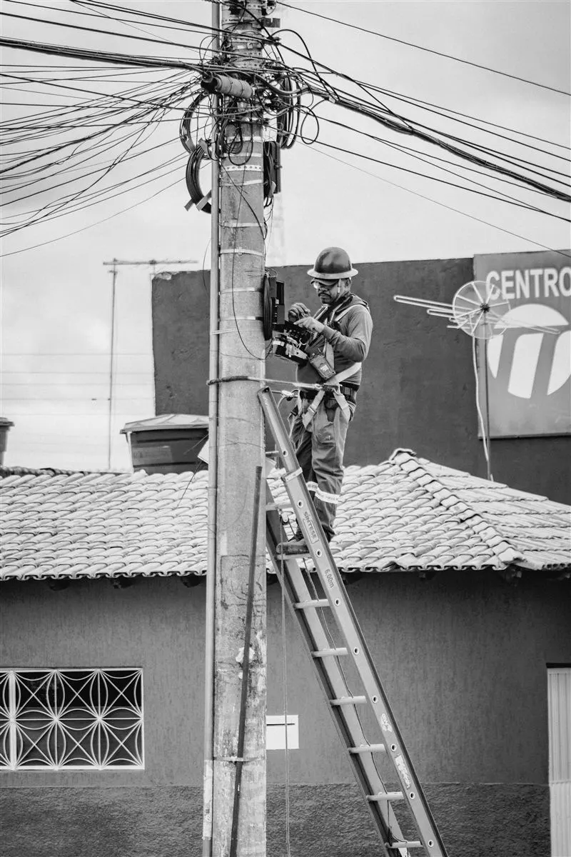 Eletricista trabalhando em poste de rede de distribuição com equipamentos de segurança